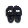 A pair of dark navy blue fuzzy slide sandals with a small Japanese flag patch on the top strap and a silver monogram logo on the footbed, shown against a plain white background.