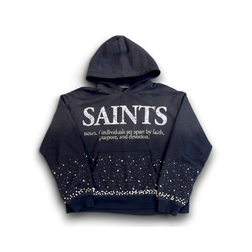 A black hoodie featuring the word 'SAINTS' printed in distressed white letters across the chest, with a dictionary-style definition underneath. The sleeves and lower body of the hoodie are decorated with white rhinestone-like star patterns, and the front pocket is lined with white rhinestones.